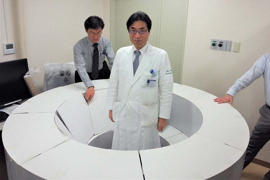 段ボールで作った実物大の模型で装置の大きさを体感する陣崎教授（2015年撮影）
