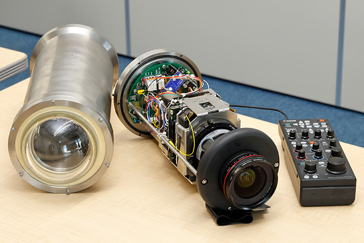 「しんかい6500」に搭載されているキヤノンの超高感度多目的カメラ「ME20F-SH」（中央）と、リモートコントローラー「RC-V100」。深度6500ｍの水圧にも耐えられるハウジング（左）に収めるため、外装は外した状態で組み込まれている